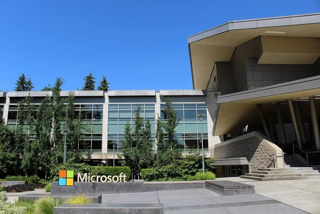 Microsoft sign in front of a building with glass windows and trees on a clear day.