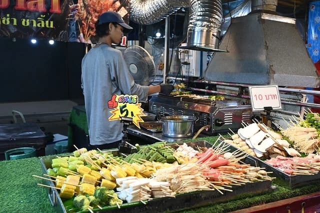 Vendor grilling skewers of vegetables and meat at a vibrant street food stall.