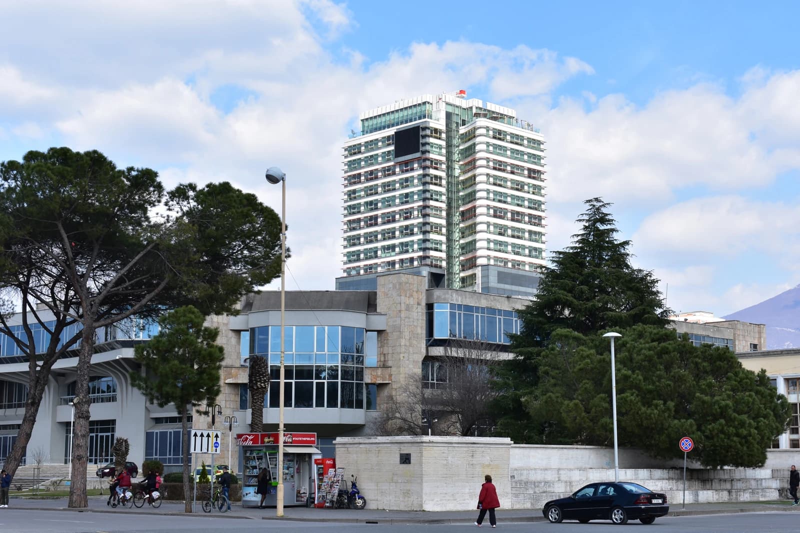 Buildings, trees, and street with a few people and cars in Tirana, Albania.