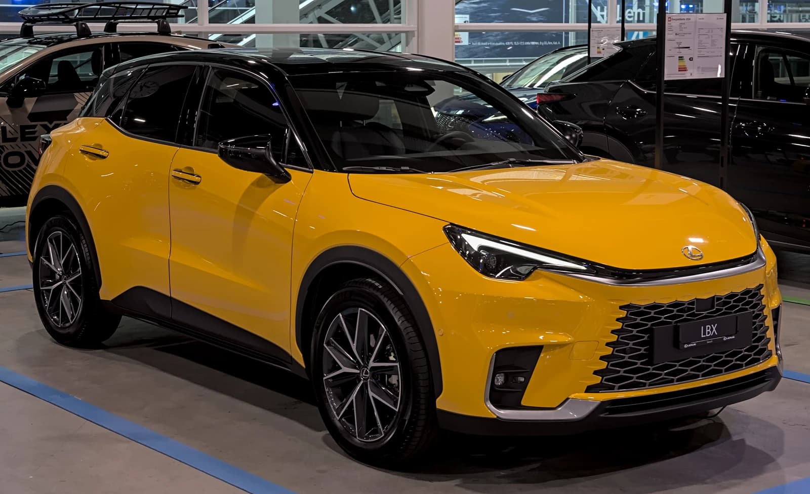 A bright yellow Lexus LBX compact SUV parked indoors at an auto show.