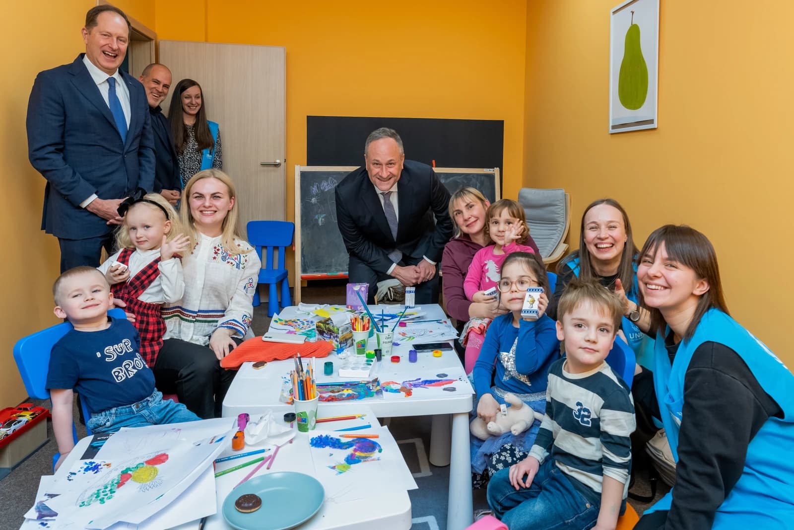 Ukrainian refugee children and adults, possibly aid workers, in a bright room.