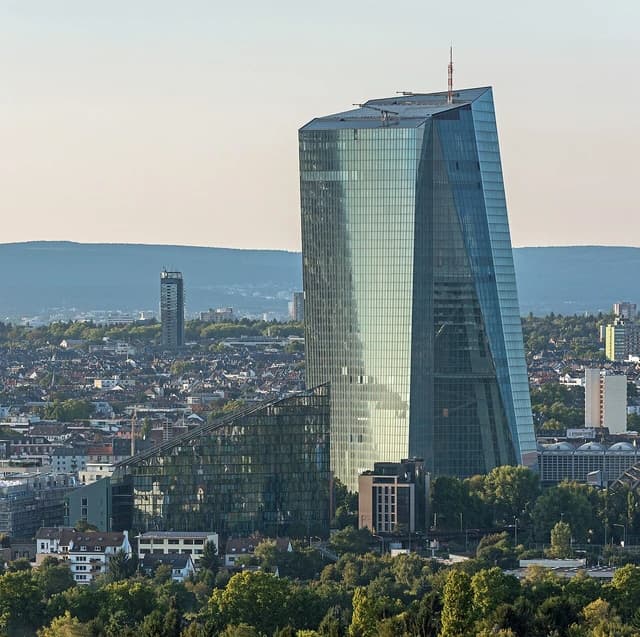 European Central Bank headquarters skyscraper with surrounding city buildings and trees.