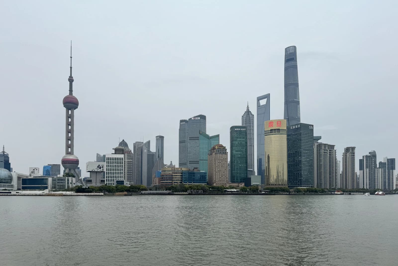 Shanghai skyline featuring the Oriental Pearl TV Tower and numerous skyscrapers along the river.
