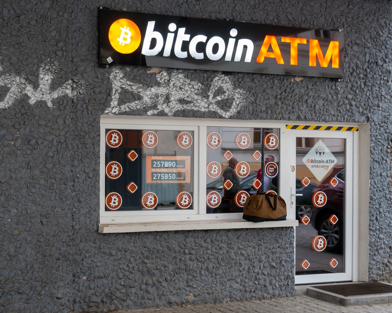 Bitcoin ATM sign on a building facade with Bitcoin logos on the windows.