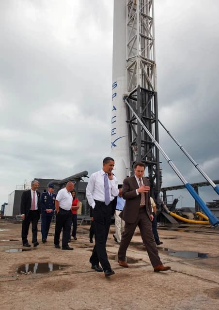President Barack Obama and Elon Musk walking at a SpaceX launch facility.