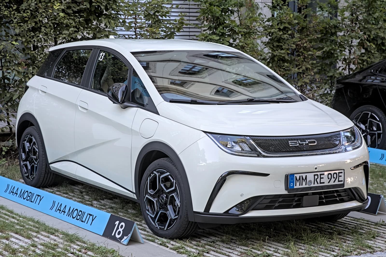 A white BYD Dolphin electric vehicle parked outdoors at a car show.