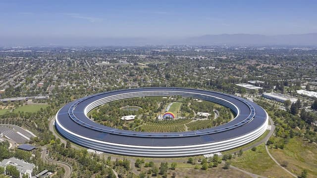 Aerial view of Apple Park, a large circular building surrounded by green landscape in Cupertino, California.