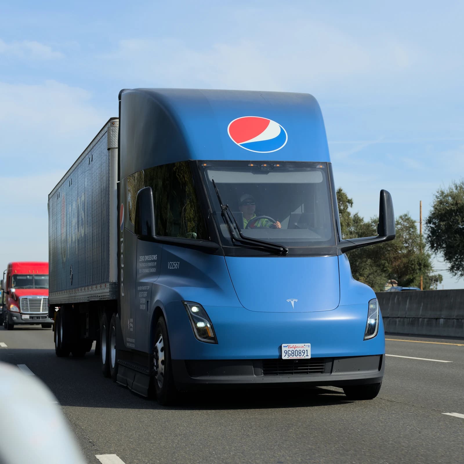 Blue Tesla Semi electric truck, branded with PepsiCo logo, driving on a highway.