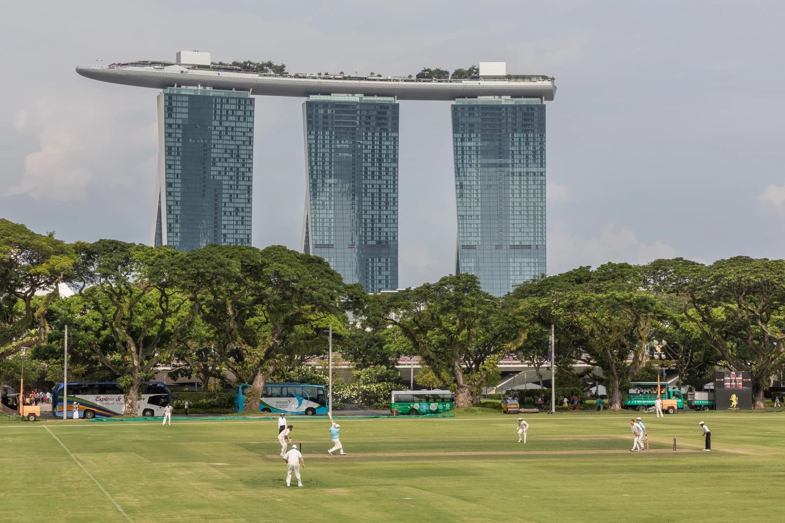 Cricket players on a green field in front of the Marina Bay Sands Hotel in Singapore.