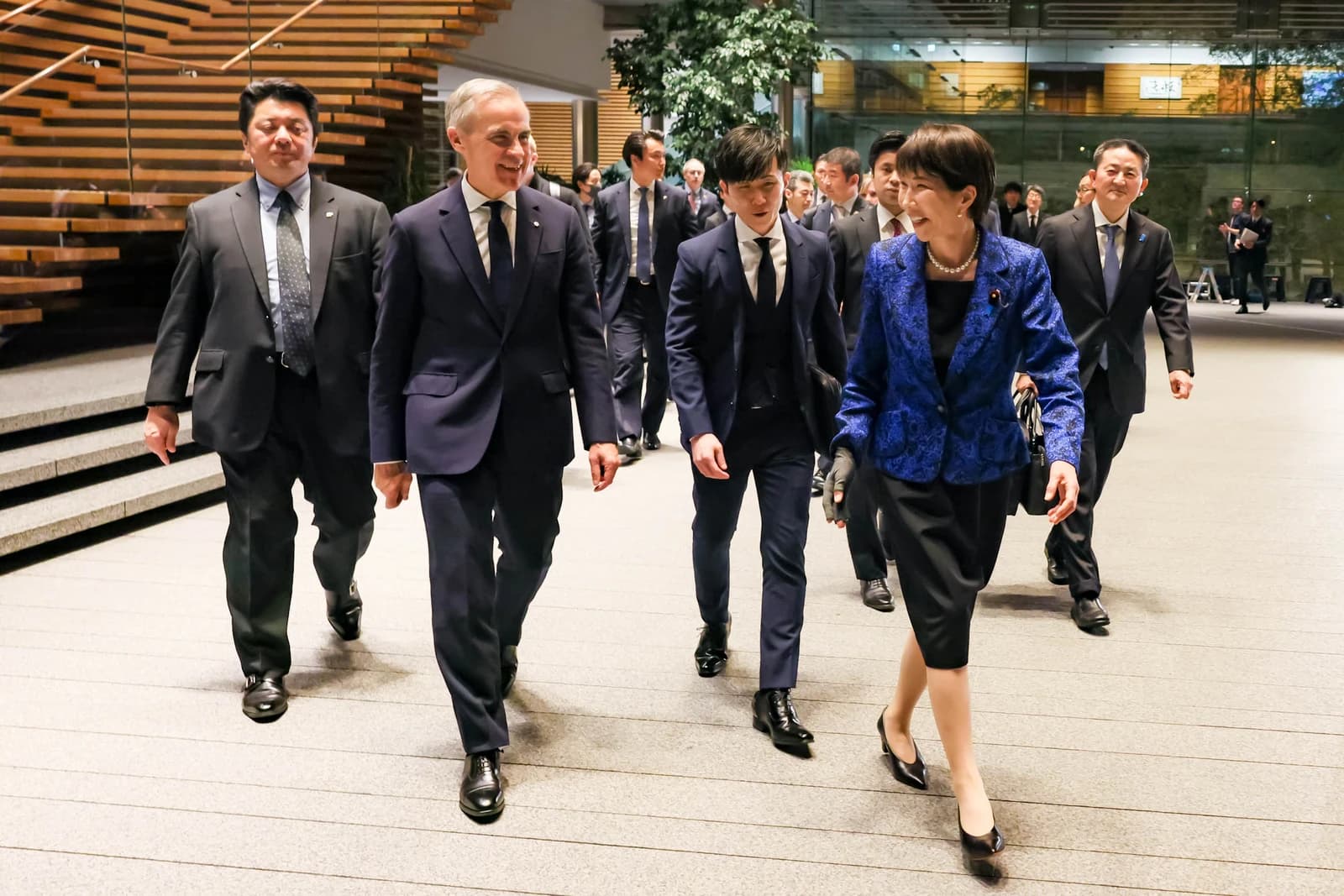 Two leaders and their entourages walking through a modern building before a working dinner.
