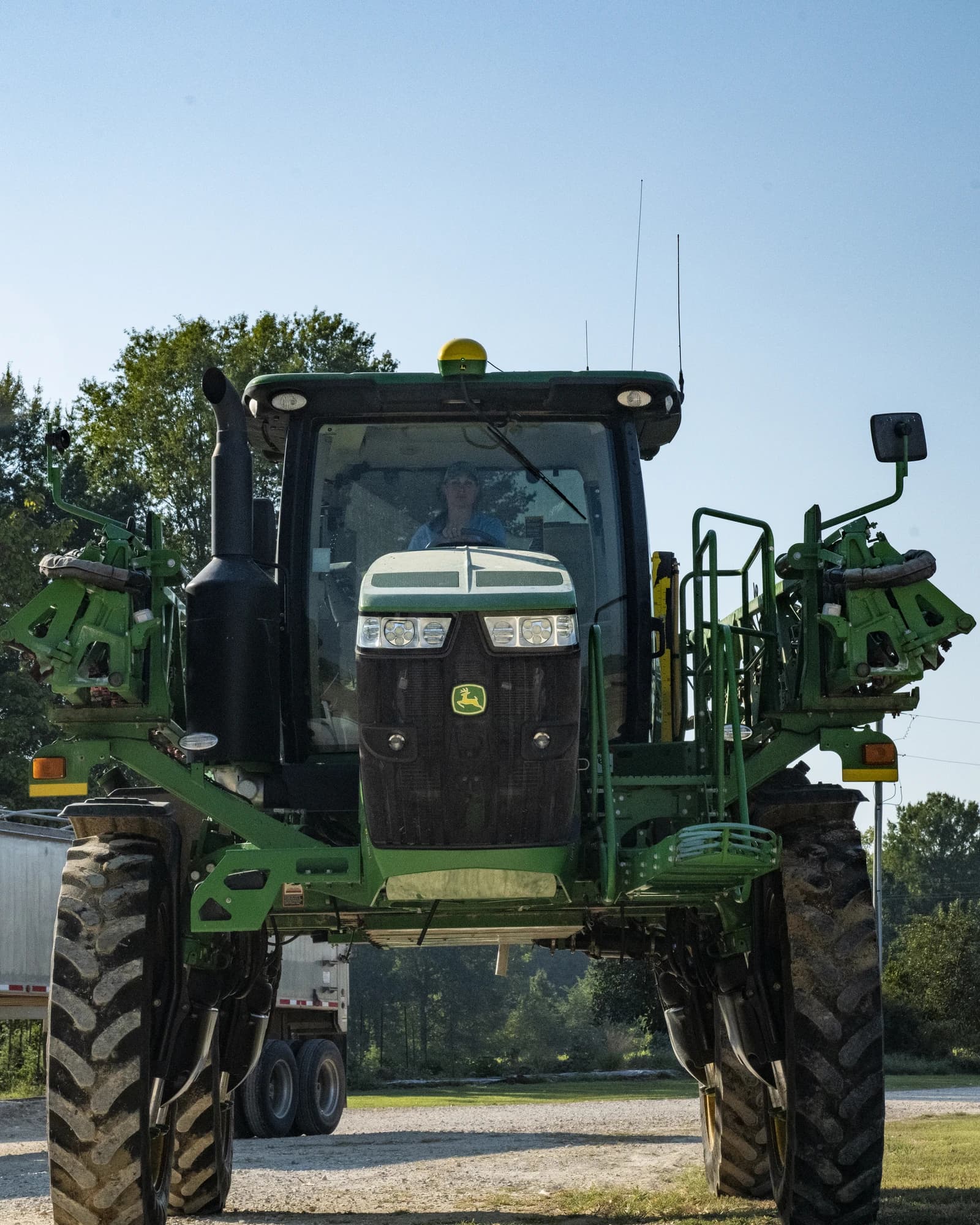 Farmer inside a John Deere tractor in a field under clear sky.