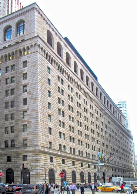 Federal Reserve Bank of New York building with people and cars on the street below.