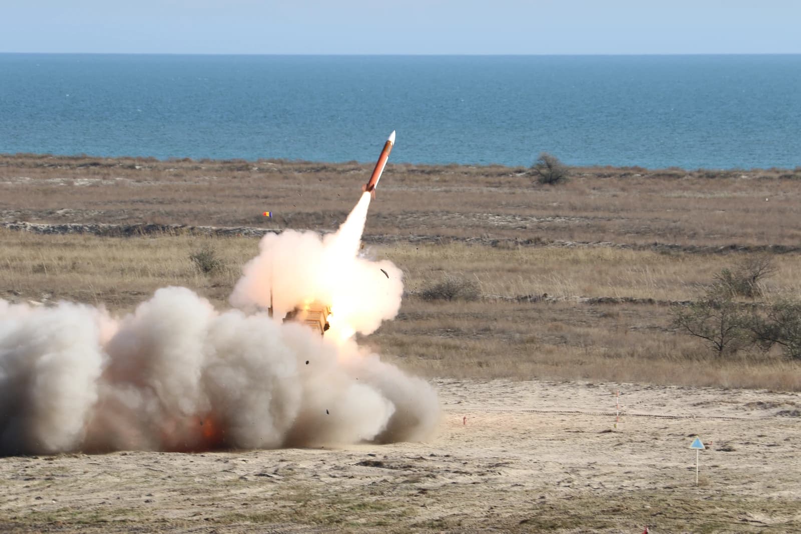 A Patriot missile launches into the sky from a ground-based system, generating significant smoke.