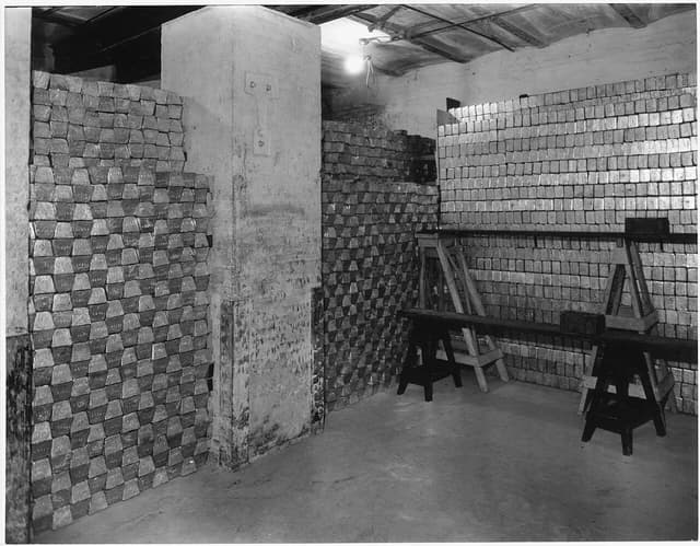 Stacks of gold bars stored inside a vault, dimly lit by a single bulb.