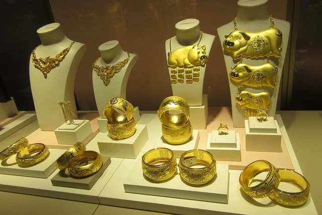 Gold necklaces, bracelets, and rings displayed on white stands in a shop.