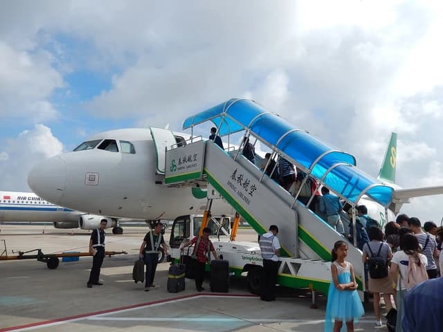 Passengers lining up to board a Spring Airlines aircraft using mobile boarding stairs.