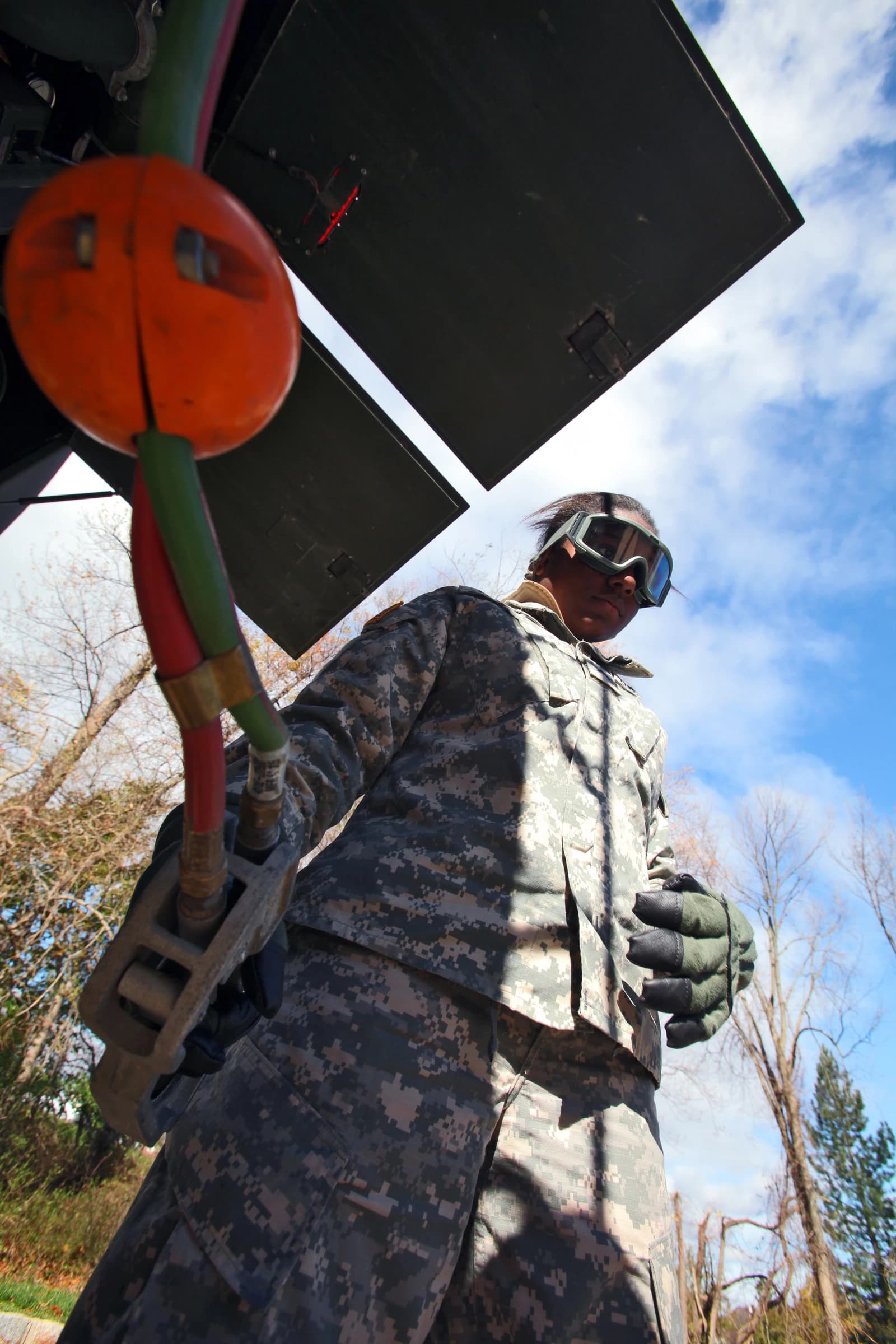An Army refueler in camouflage and goggles holding a fuel nozzle.