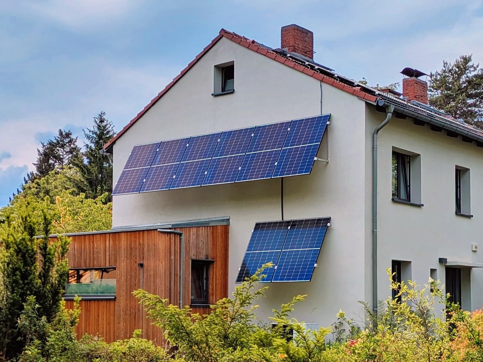 Photovoltaic panels installed on the side of a residential building surrounded by green trees.
