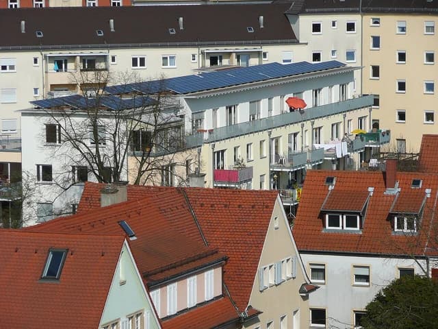 Photovoltaic panels installed on the flat roofs of multiple apartment buildings in a city setting.