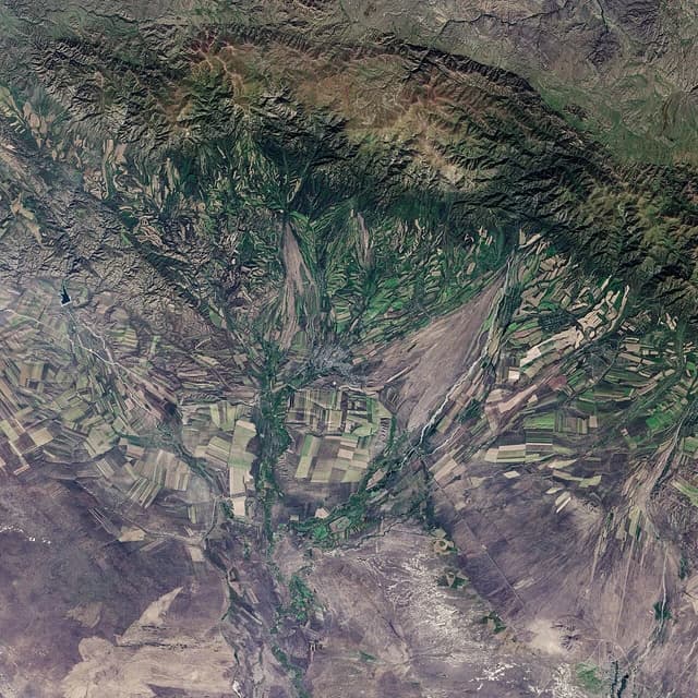 Aerial view of green and brown agricultural fields across mountainous landscape in Kazakhstan.