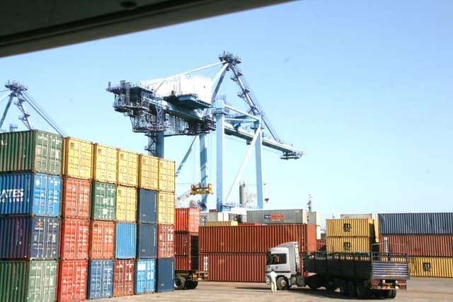 Shipping containers stacked at Mombasa port with large cranes overhead.