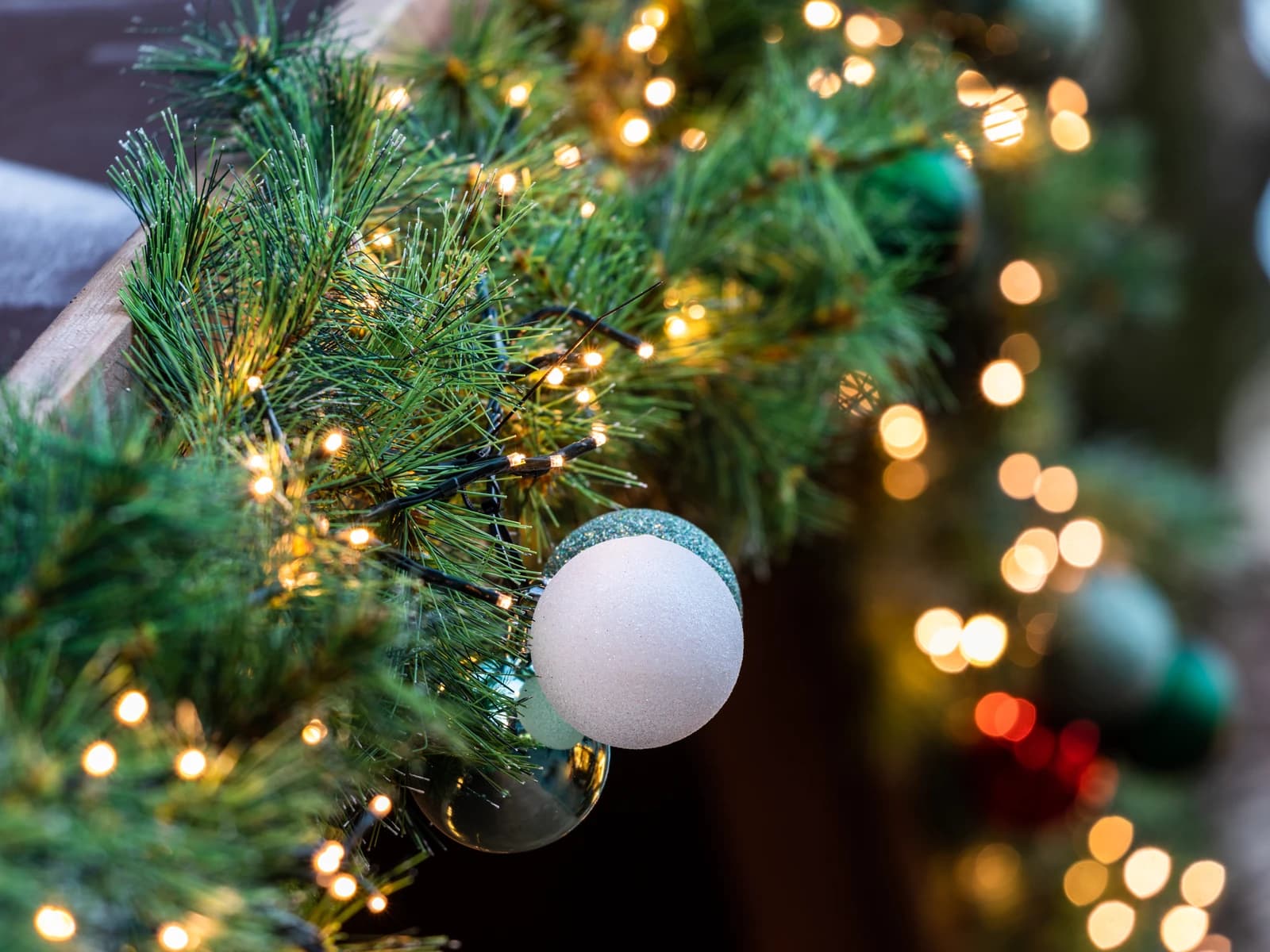 Close-up of pine garland adorned with festive string lights and ornaments.