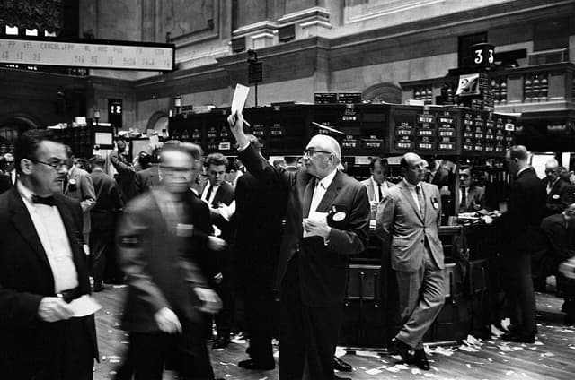 New York Stock Exchange traders working on the trading floor, one raising a paper in the air.