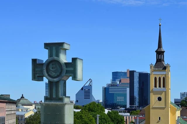 Cross of Liberty monument and a church steeple in the Tallinn skyline on a clear day.