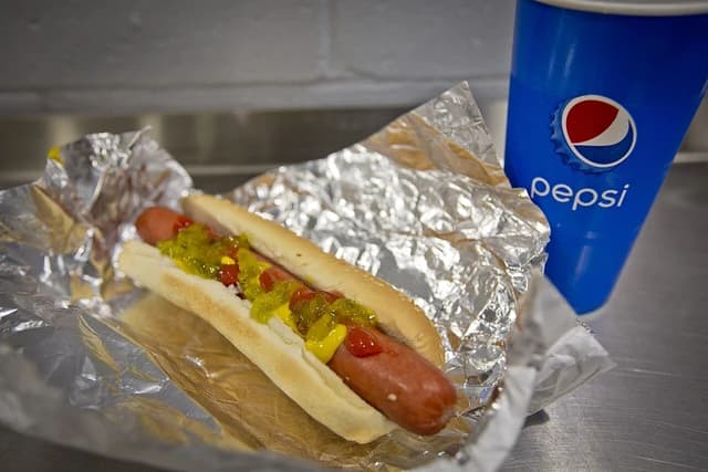Costco hot dog with relish and mustard next to a blue Pepsi cup.