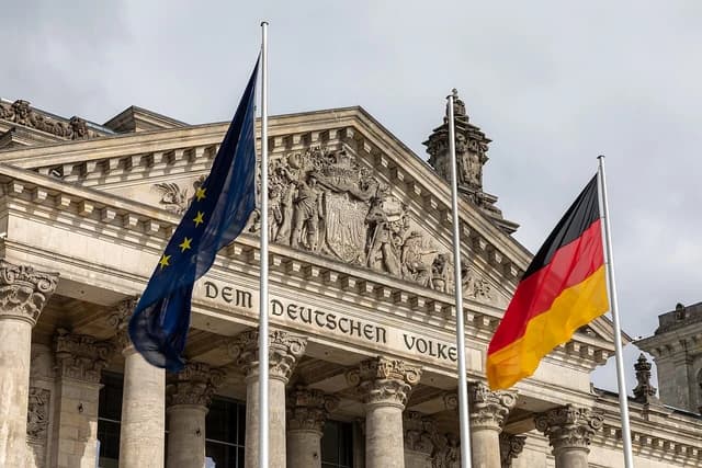 German and European Union flags flying in front of the Reichstag Building in Berlin.
