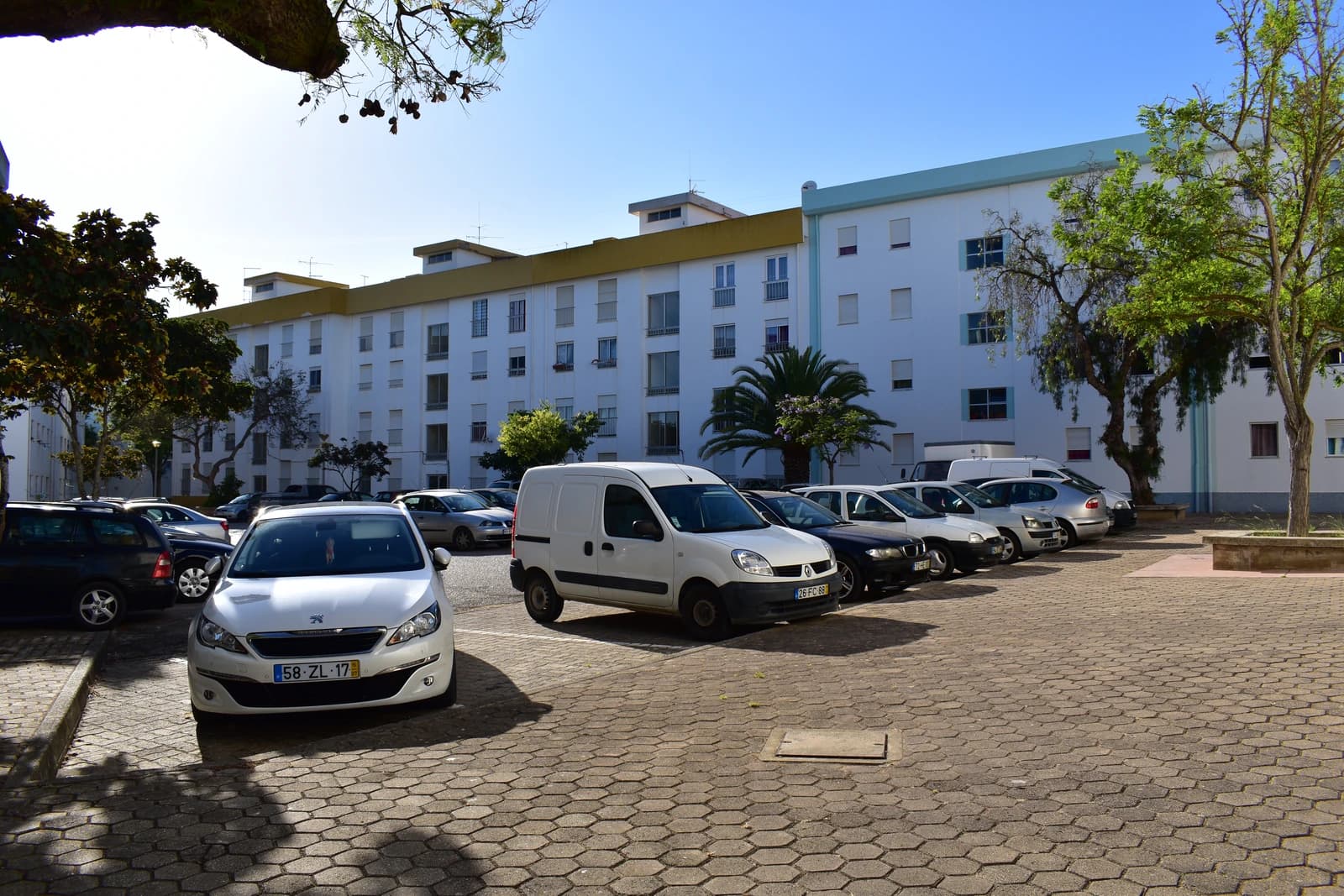 Apartment buildings with multiple floors and cars parked on a paved lot in front.