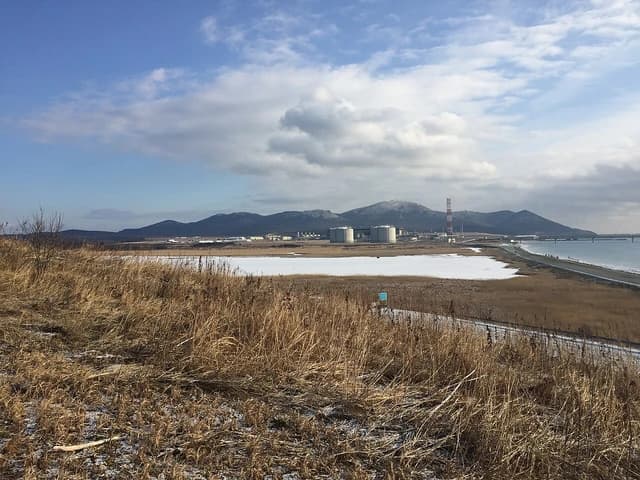 Prigorodnoye production complex with large LNG storage tanks and industrial facilities next to a body of water.