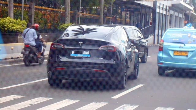 A black Tesla Model Y driving on a busy city street.