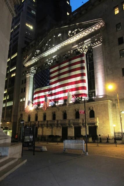 New York Stock Exchange building illuminated at night with a large American flag displayed.