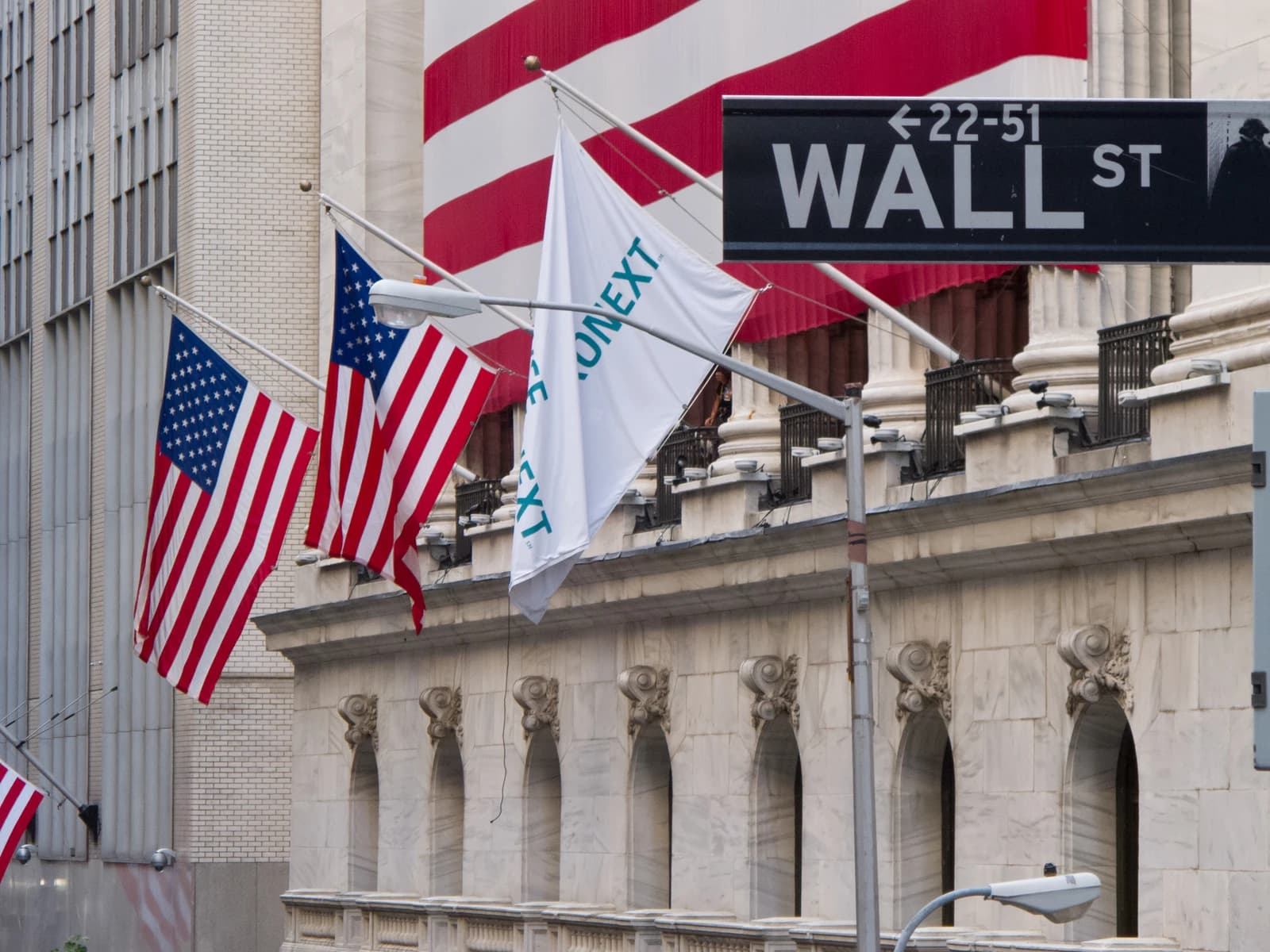 Wall Street sign with American flags displayed on a building in New York City.