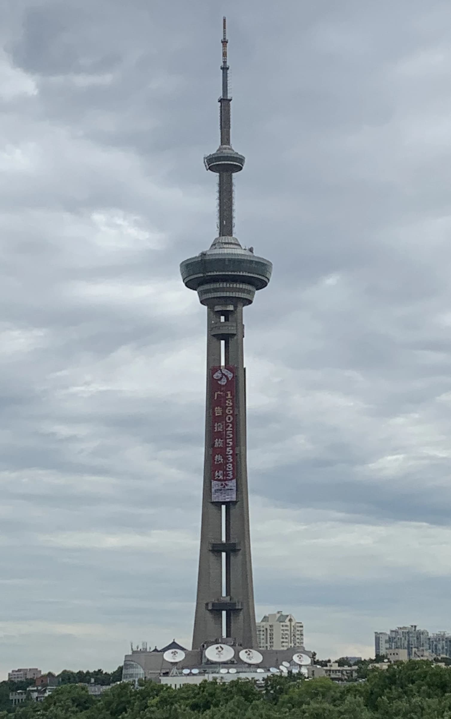 Nanjing TV Tower, a tall concrete structure with broadcasting equipment, under a cloudy sky.