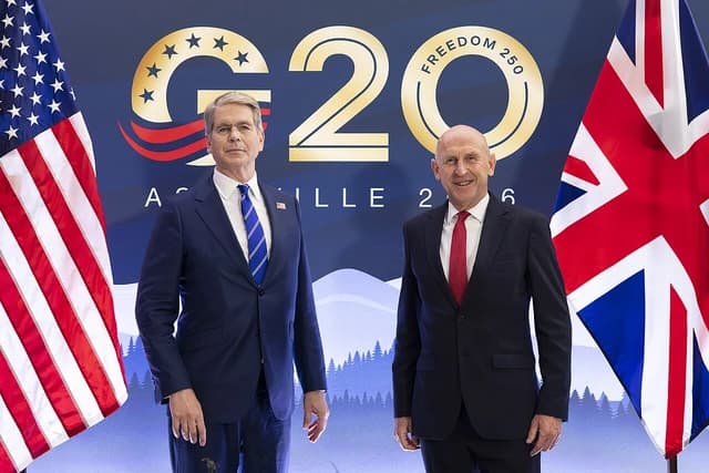 John Healey, UK Chancellor, stands next to a podium with flags.