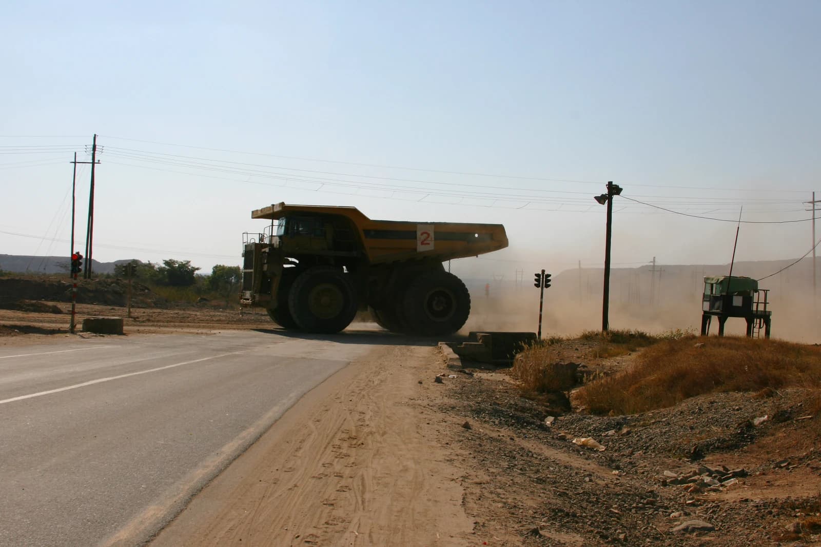 A massive yellow mining haul truck driving on a dirt track in a dusty landscape.