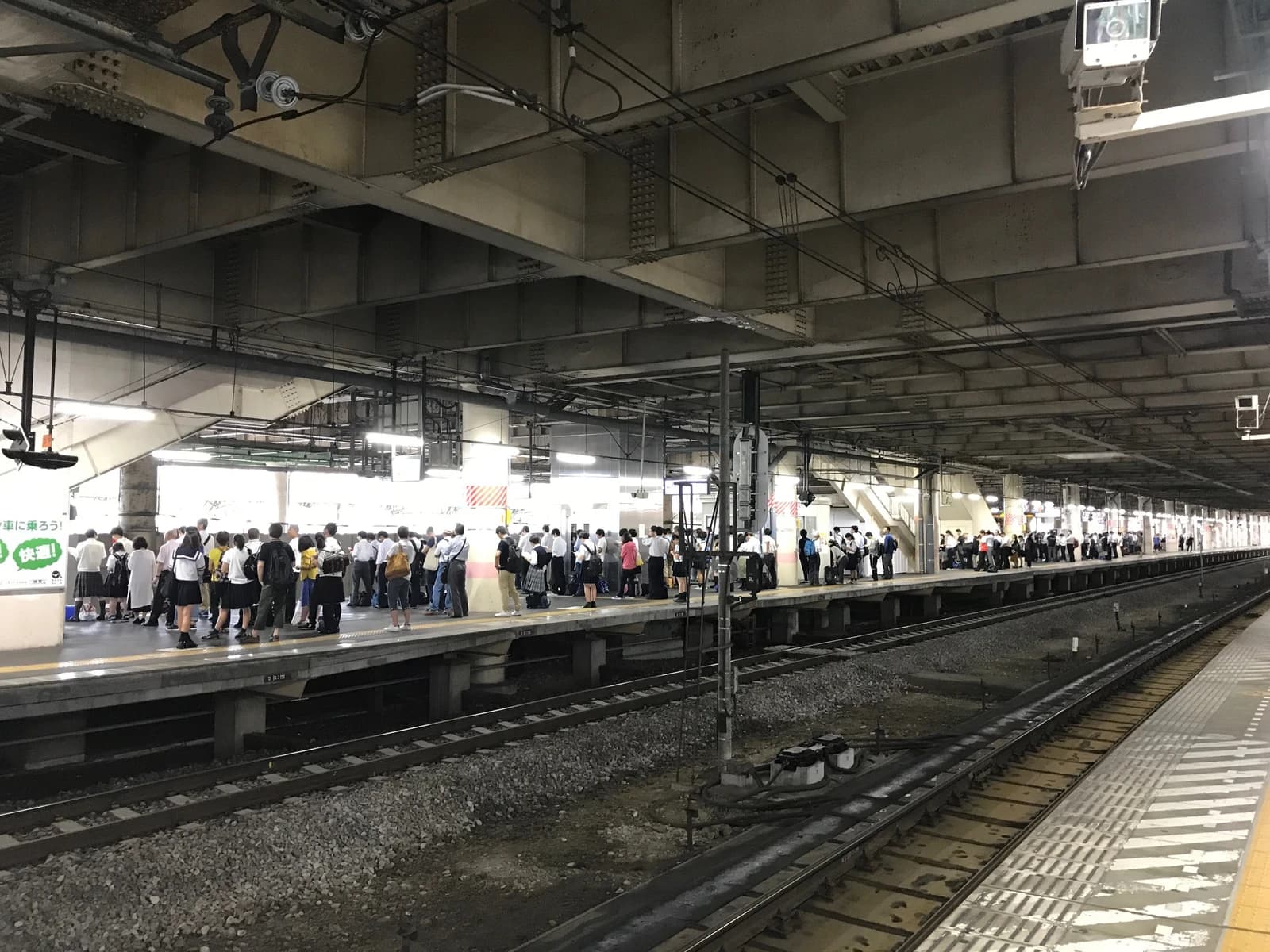 People standing on a long, busy train platform at Kumagaya Station, looking down the tracks.