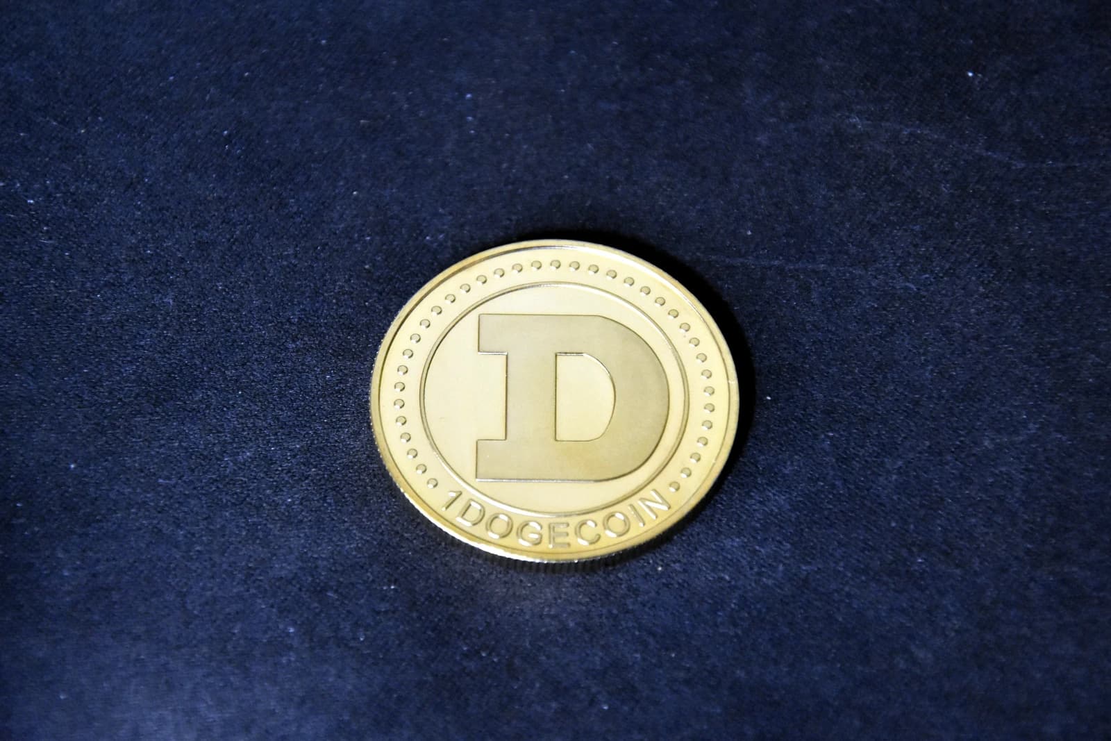 A gold-colored physical Dogecoin with a large 'D' and '1 DOGECOIN' on its surface.