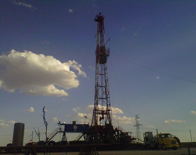 An oil drilling rig, Paterson Rig Number 623, stands under a partly cloudy sky.