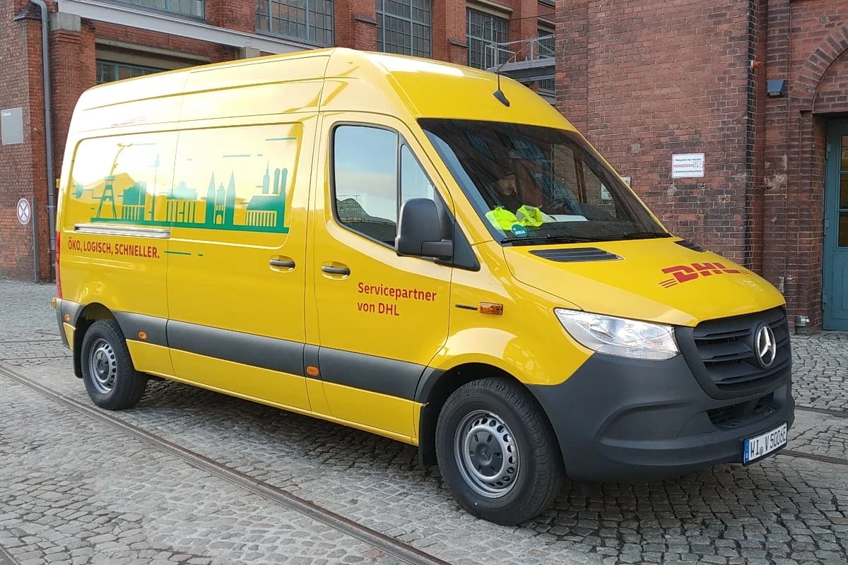 A yellow DHL Mercedes-Benz eSprinter delivery van parked outside a brick building.