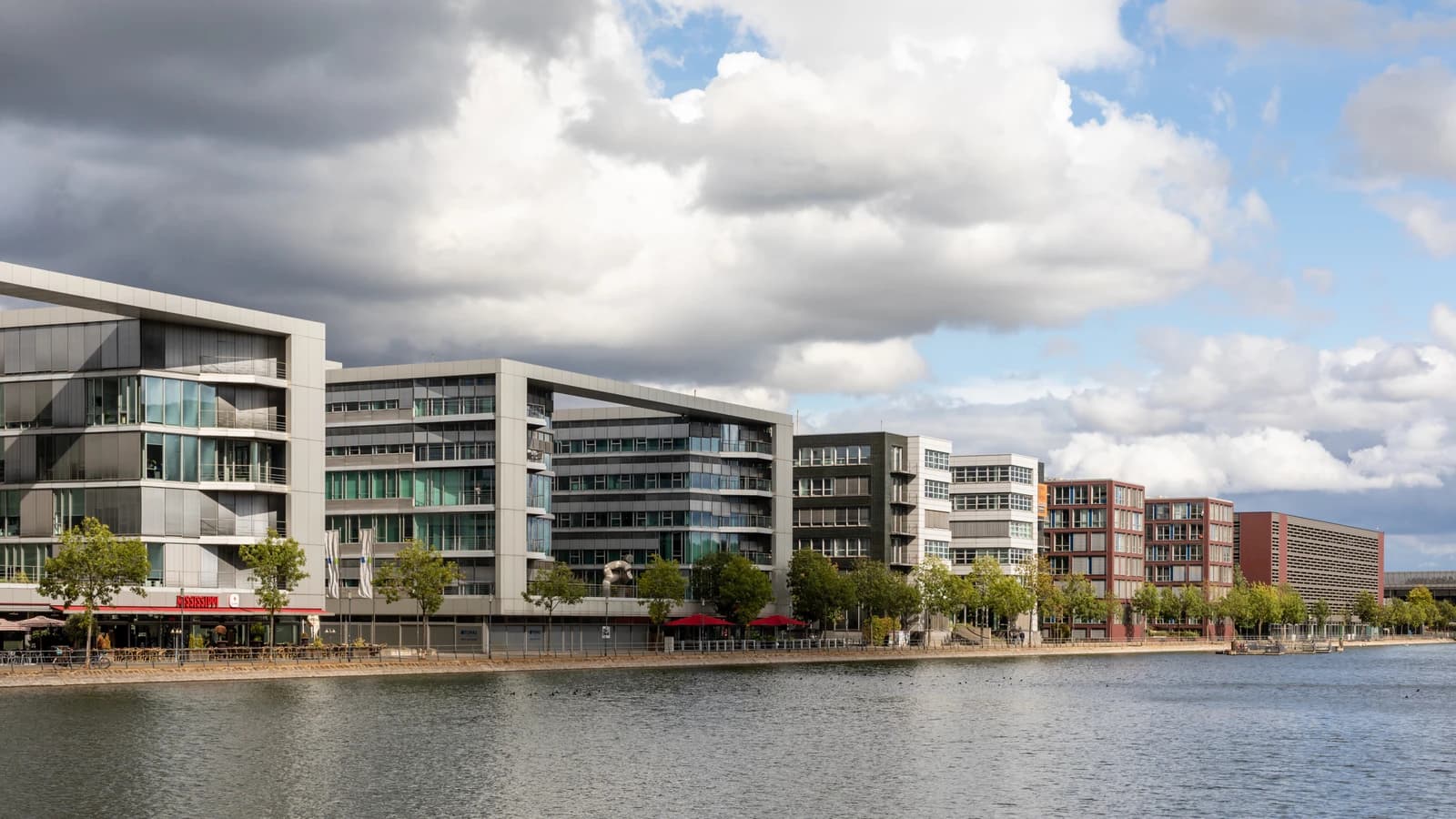 Modern office buildings with glass facades and balconies situated along a body of water.