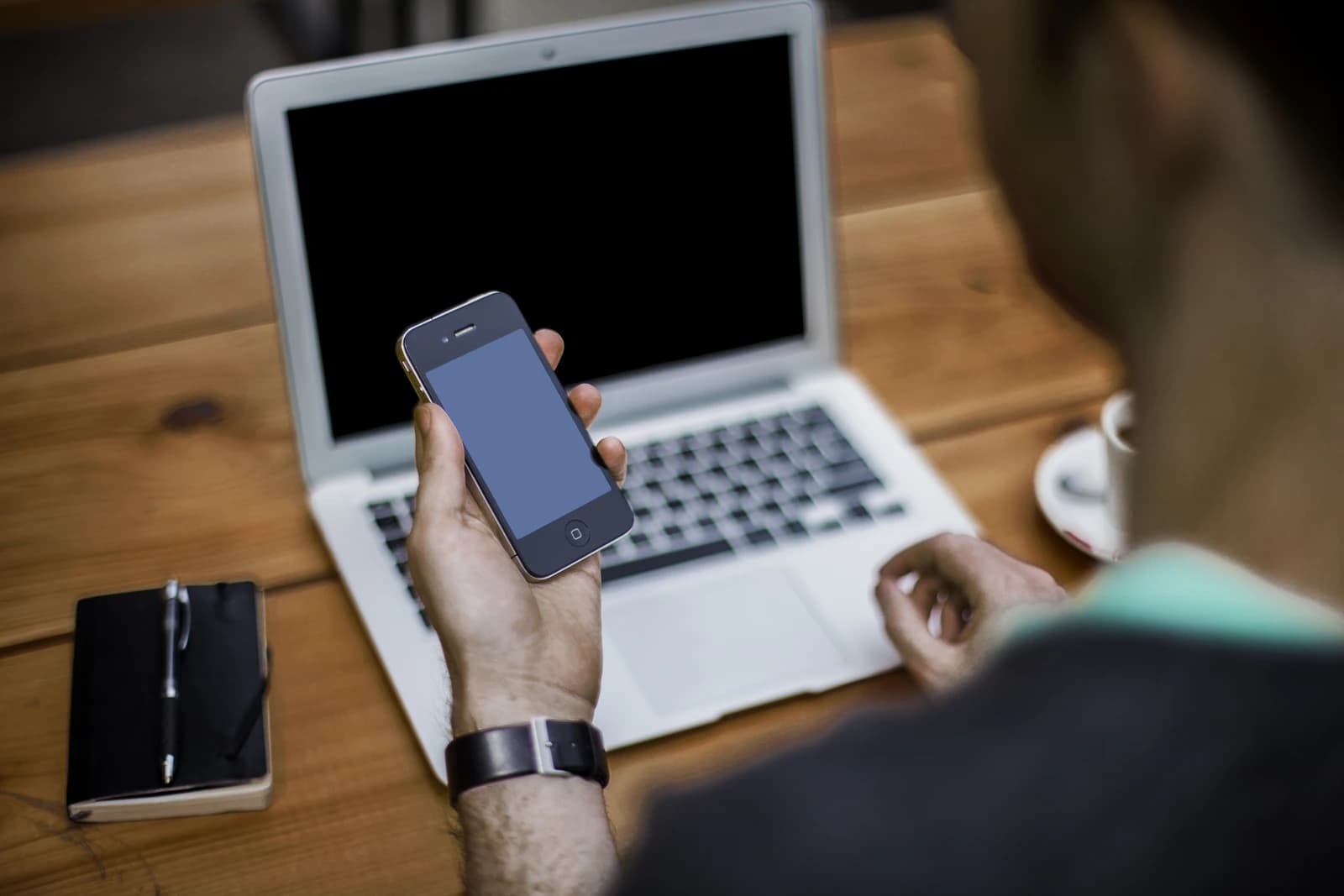 Man's hand holding a smartphone in front of an open laptop.