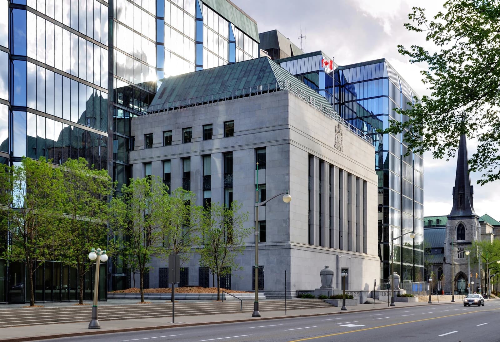 Exterior view of the Bank of Canada building with glass towers behind it.