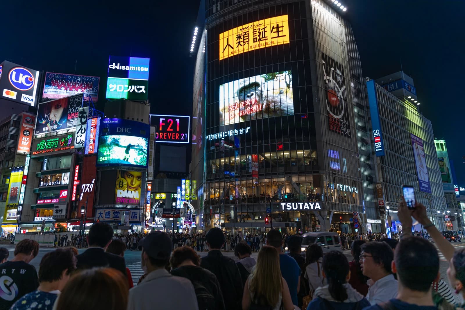 Pedestrians and cars at night at Shibuya Crossing in Tokyo, Japan, with bright neon signs.