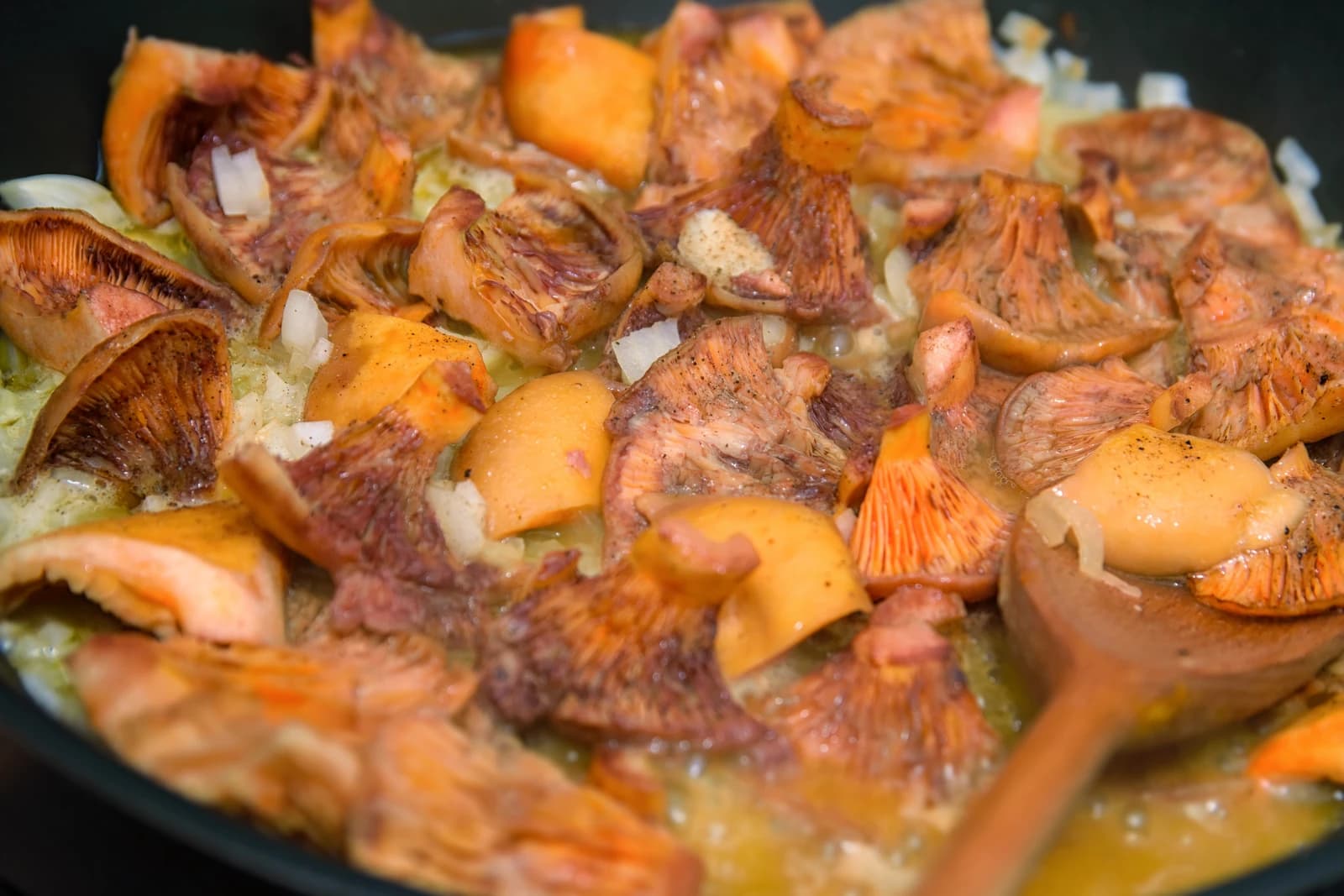 Red pine mushrooms and chopped onions cooking in a black frying pan.