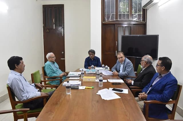 Five men in business casual attire seated around a conference table with documents and water bottles.