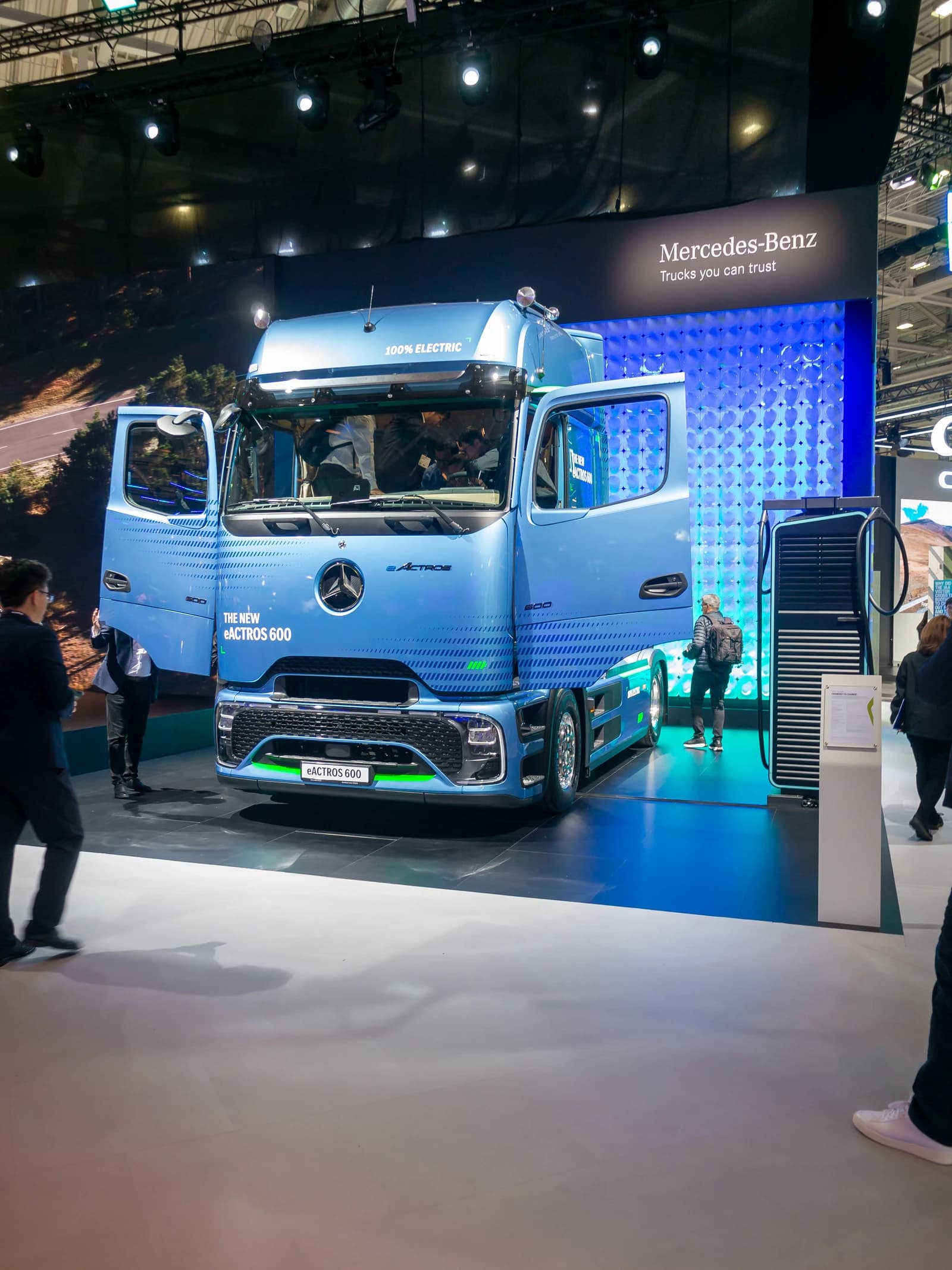 A blue Daimler Truck eActros 600 is displayed at an exhibition hall.