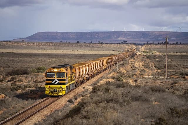 Aurizon iron ore train travels through a remote landscape with wind turbines in the distance.